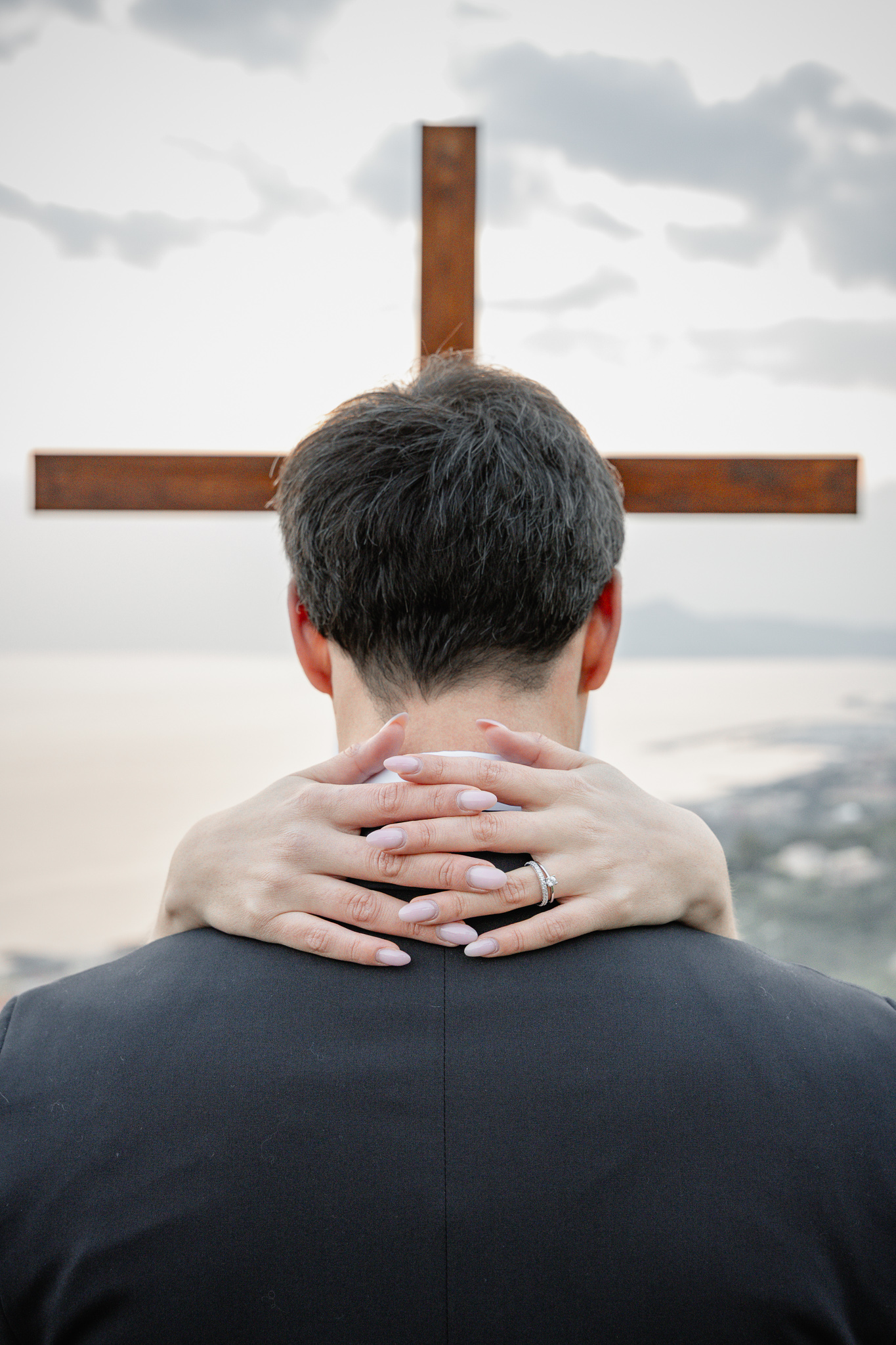 Dettaglio della sposa che abbraccia lo sposo davanti alla croce durante matrimonio cristiano evangelico in Liguria con vista panoramica sul mare.